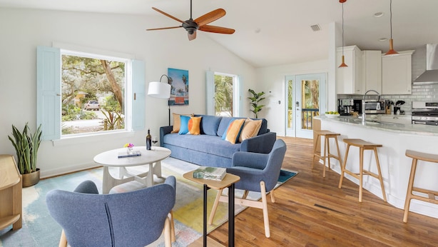 A modern living room with a blue sofa, wooden floor, and a ceiling fan.