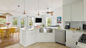 A modern kitchen with white cabinetry, a built-in dishwasher, a stove, and a dining area with yellow chairs and a wooden table.