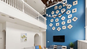 Een ruime woonkamer met een grote grijze hoekbank, een kroonluchter, een flatscreen-tv en een blauwe accentmuur met decoratieve houten cirkels.