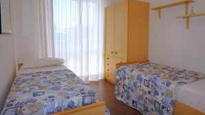 A bedroom with two beds, a wooden wardrobe, and a window with sheer curtains.