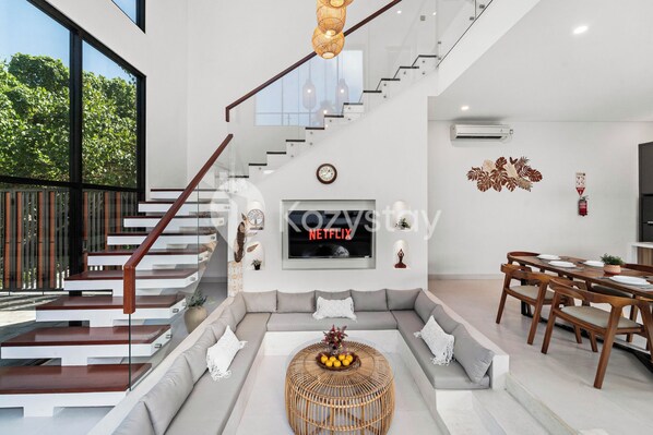 Una sala de estar moderna con una escalera, un comedor y un ventanal con vistas a zonas verdes.