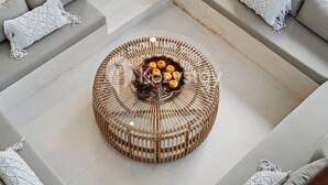A modern living room with a round woven coffee table, grey sofas, and white crocheted cushions. - Kleio Villa by Kozystay - Canggu (Canggu)