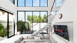 A modern living room with a large TV, a staircase, and a balcony with plants. - Kleio Villa by Kozystay - Canggu (Canggu)