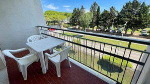 Ein Balkon mit weißem Tisch und Stühlen, mit Blick auf einen Parkplatz und Grünflächen.