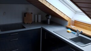Ett modernt kök med ett takfönster, mörka skåp, en vit bänkskiva och en diskho i rostfritt stål.