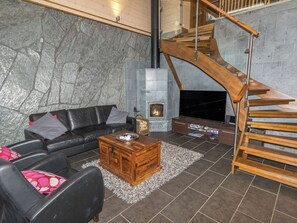 Un salon moderne avec un mur en pierre, un canapé en cuir noir, une table basse en bois et une cheminée avec un téléviseur.