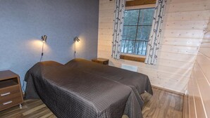 Ein Schlafzimmer mit zwei Betten, Holzboden, einem Fenster mit gemusterten Vorhängen und Wandleuchten.