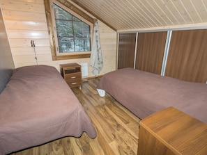 A cabin with two beds, a small wooden nightstand, a window with a view of trees, and a wooden ceiling. - Unelmarakka b by Interhome (Kittilä)