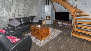 Ein modernes Wohnzimmer mit Steinwand, Kamin, schwarzem Ledersofa, Couchtisch aus Holz und einer Holztreppe.