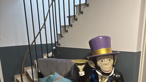 A staircase with a modern design, a grey sofa with a blue cushion, and a statue of a character holding a hat. - Room 'Haus Erika 1' with Shared Terrace and Wi-Fi (Lingen (Ems))