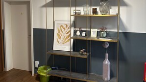 A room with a wooden floor, a glass display unit with various items, a green trash bin, and a fire extinguisher. - Room 'Haus Erika 1' with Shared Terrace and Wi-Fi (Lingen (Ems))