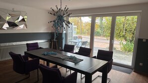 A dining area with a table and chairs, a decorative ceiling light, and a view of the outdoors through large windows. - Room 'Haus Erika 1' with Shared Terrace and Wi-Fi (Lingen (Ems))