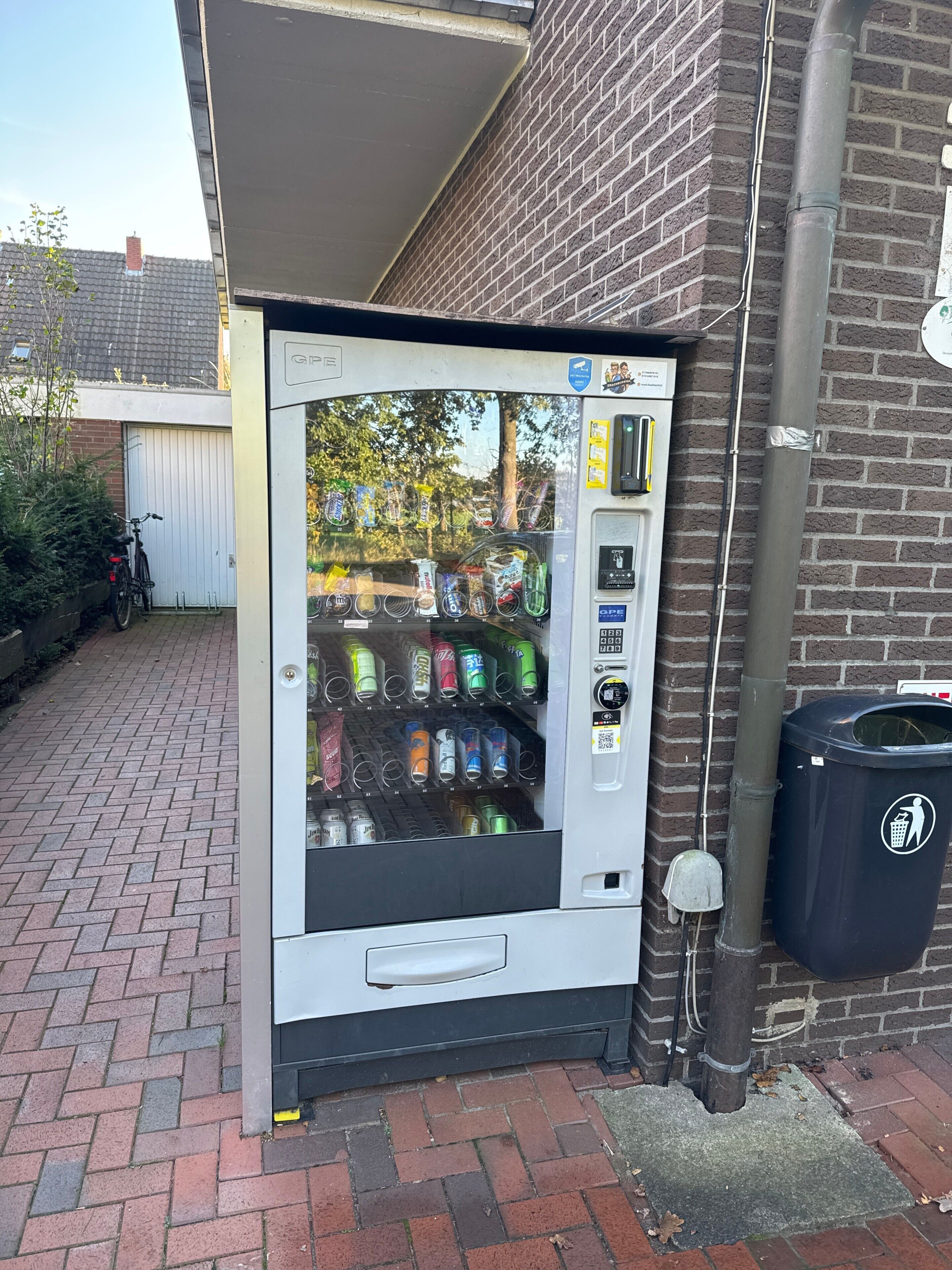 Ein Getränkeautomat mit verschiedenen Getränken und ein Mülleimer daneben.