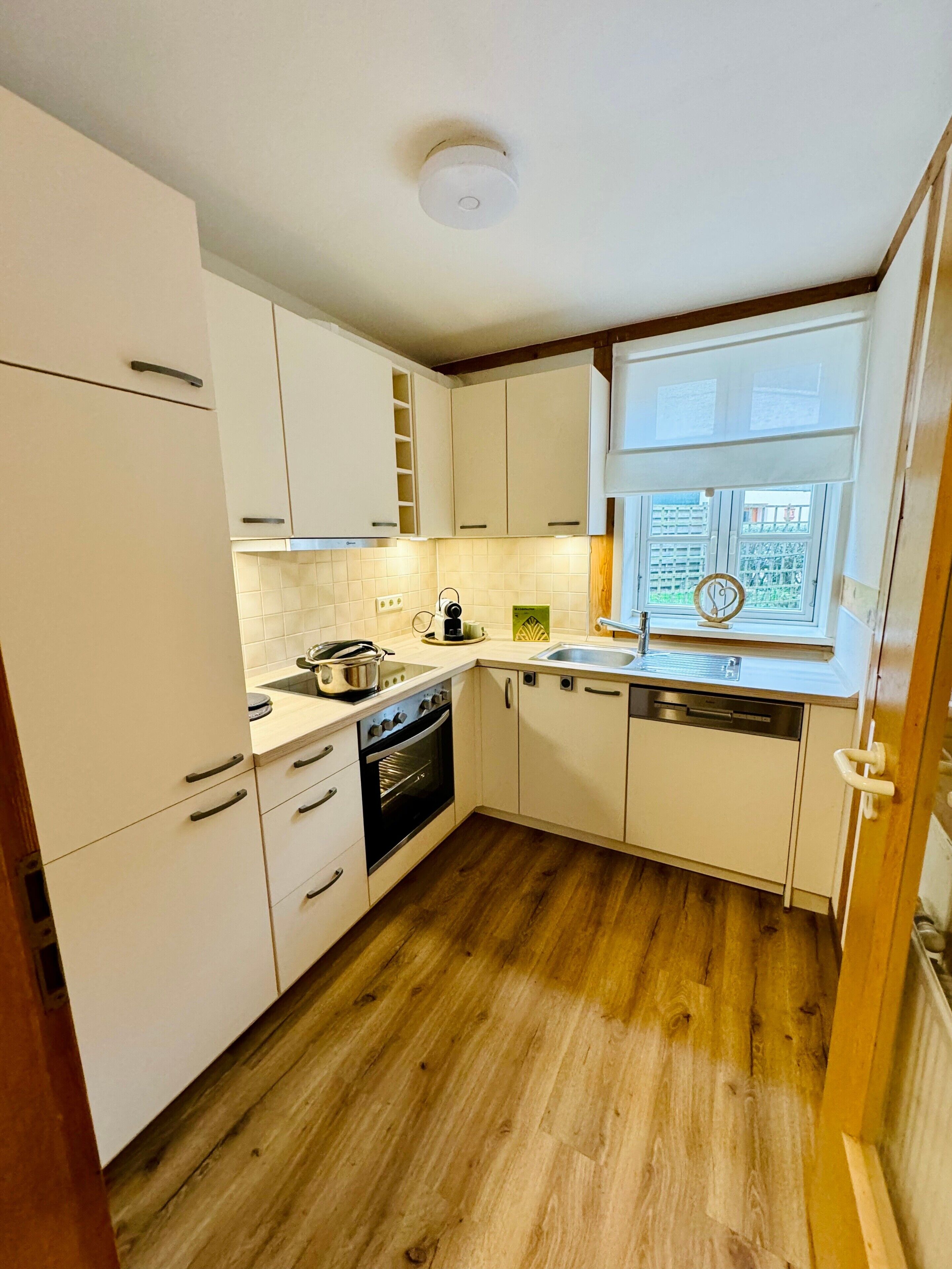 A compact kitchen with white cabinets, a stove, oven, sink, and a window with a view.