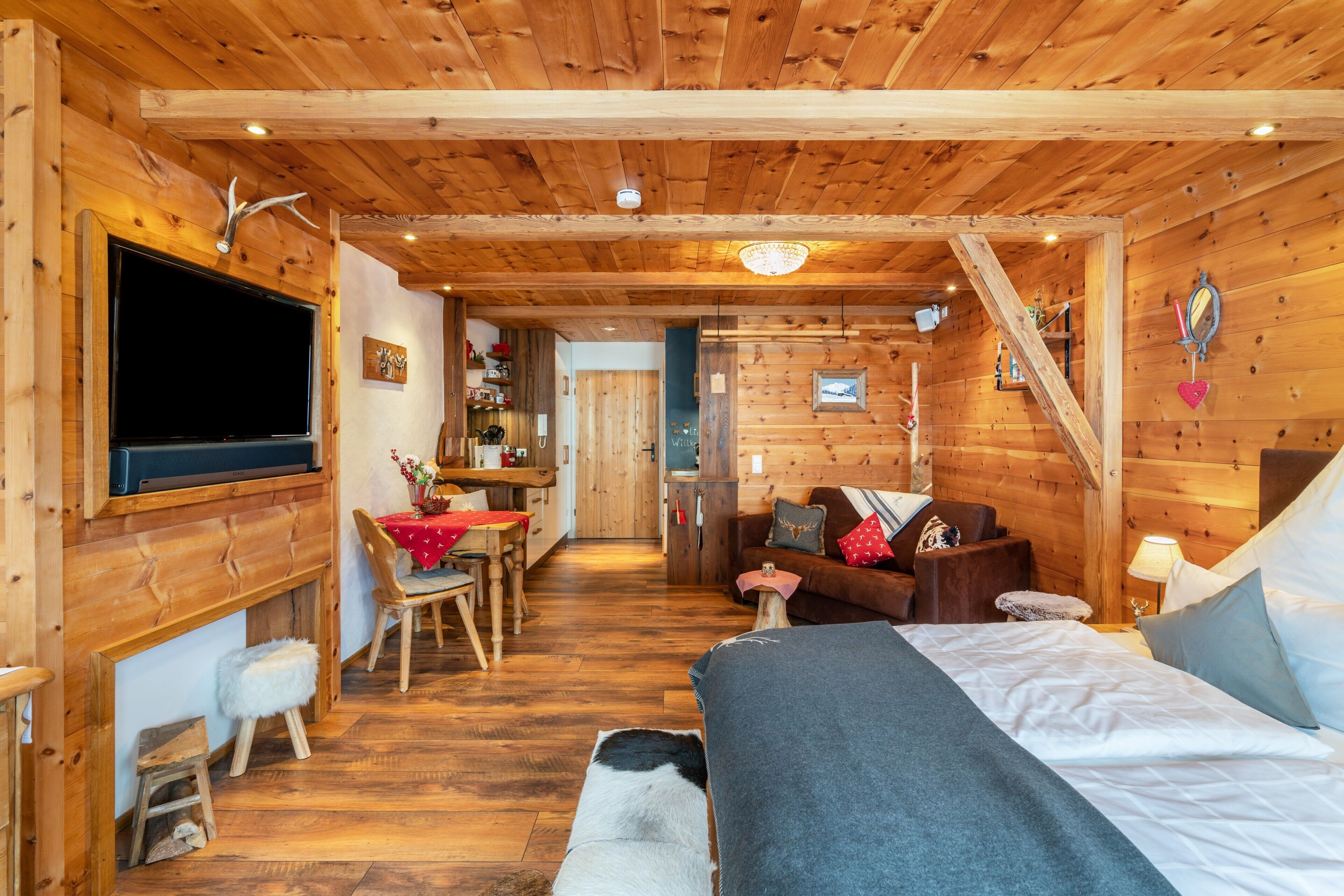 Interior de una cabaña de madera con cama, televisor, comedor y cocina.