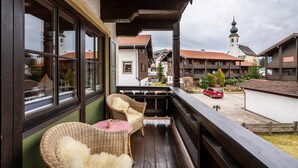 A balcony with wicker chairs and a table, overlooking a street with buildings and a church tower. - Studio Apartment "Chalet Bergliebe Inzell mit Zirbenholz" with Mountain View & Wi-Fi (Inzell)