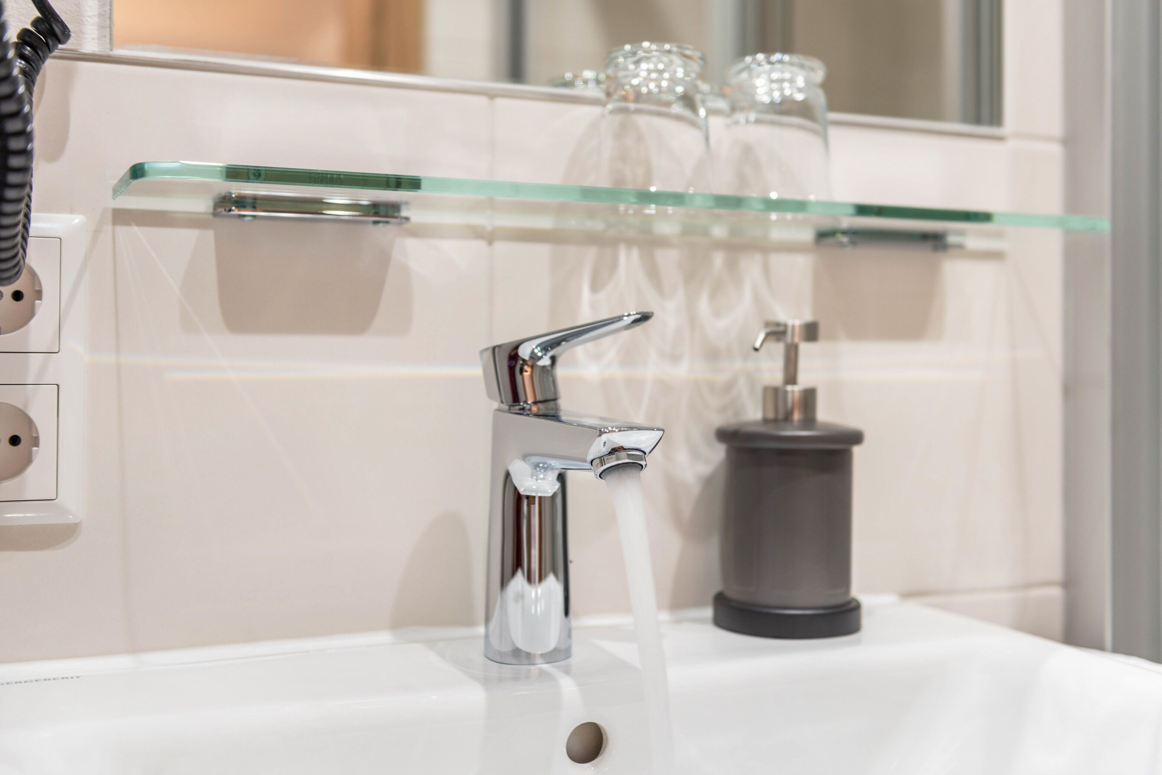 A bathroom with a modern faucet, a glass shelf with toiletries, and a mirror.