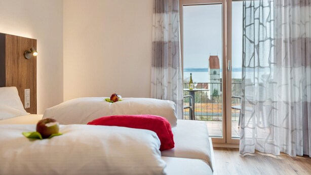 A hotel room with a bed, a window with curtains, and a view of the outside.