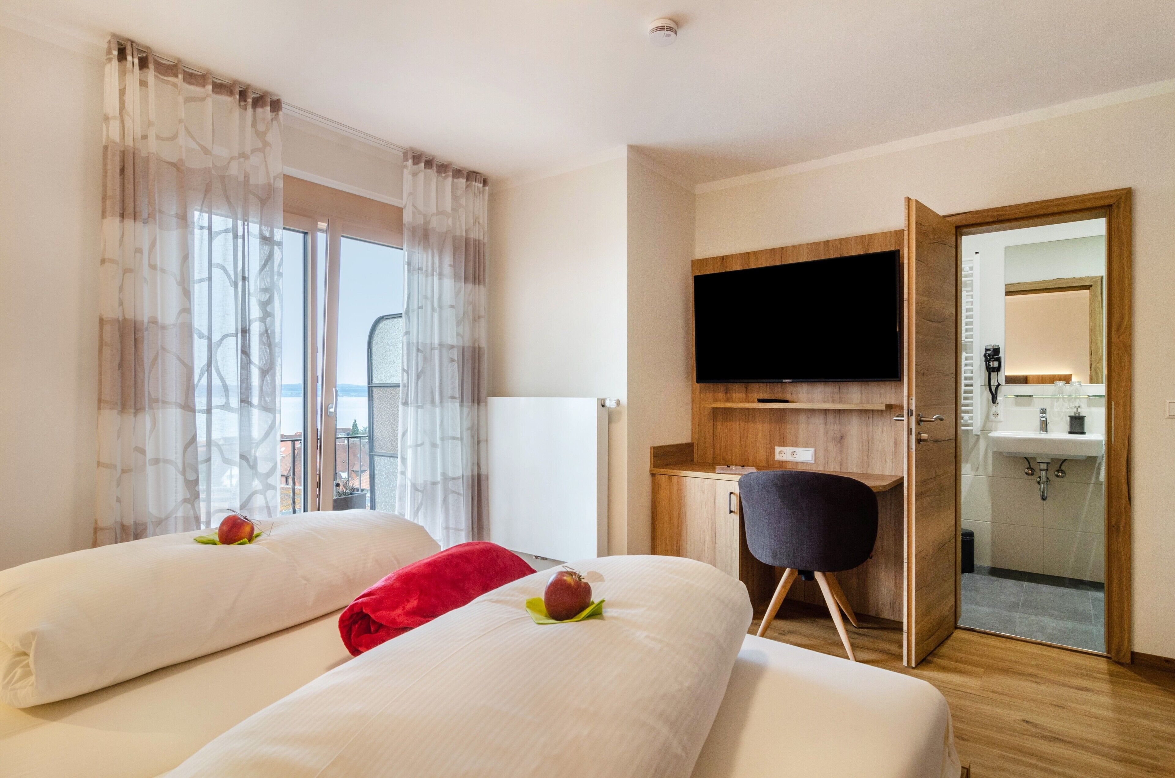 Camera d'albergo con due letti, televisione, scrivania e bagno visibile attraverso una porta aperta.