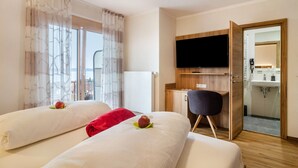 A hotel room with two beds, a TV, a desk, and a bathroom visible through an open door.
