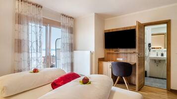 Camera d'albergo con due letti, televisione, scrivania e bagno visibile attraverso una porta aperta.