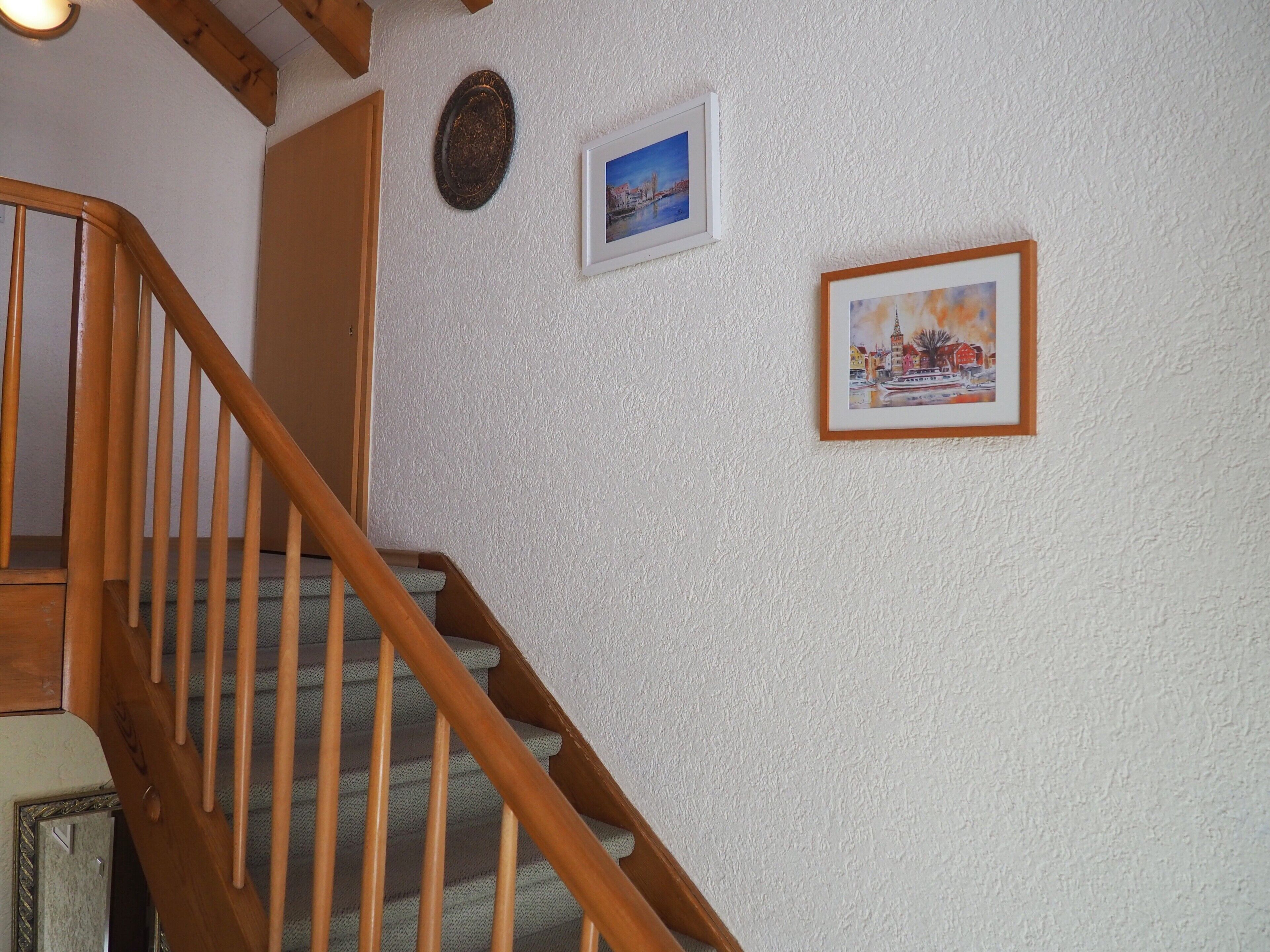 Una scala in legno con un muro strutturato, un quadro con una veduta urbana e un quadro con una scena invernale.