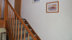 A wooden staircase with a textured wall, a framed picture of a cityscape, and a framed picture of a winter scene. - Double Room with Lake View, Balcony and Wi-Fi (Hagnau am Bodensee)