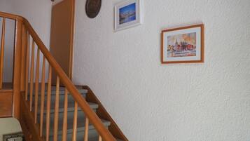 Una scala in legno con un muro strutturato, un quadro con una veduta urbana e un quadro con una scena invernale.