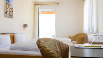 A hotel room with a bed, a wicker chair, a desk with a laptop, and a window with curtains.