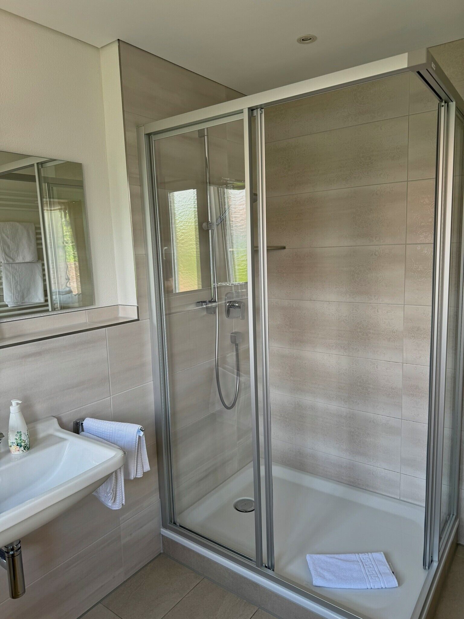 Ein modernes Badezimmer mit einer gläsernen Duschkabine, einem Waschbecken mit Handtuch und einem Spiegel.