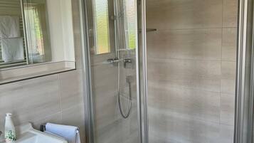 Ein modernes Badezimmer mit einer gläsernen Duschkabine, einem Waschbecken mit Handtuch und einem Spiegel.