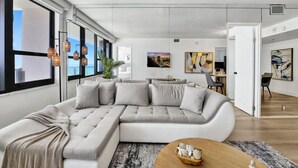 A modern living room with a large L-shaped sectional sofa, a coffee table, and a view through large windows. - Beautiful Oceanview Condo 2 Bedrooms, 2 Bathrooms with Beach Service 709 (Miami Beach)