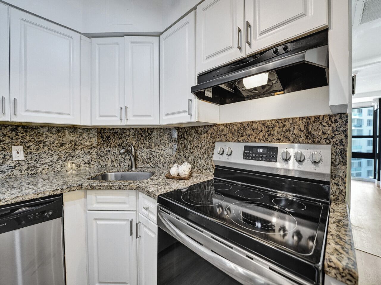 A kitchen with white cabinets, a granite countertop, a stainless steel dishwasher, and a four-burner stove.