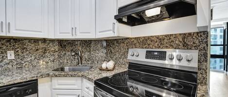 A kitchen with white cabinets, a granite countertop, a stainless steel dishwasher, and a four-burner stove.