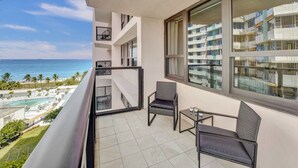 A balcony with a view of the ocean, a pool, and a building in the background. - Luxury Beach Condo with Exclusive Resort Amenities 1016 (Miami Beach)