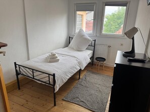 A small, single-bed room with a window, a radiator, a desk with a lamp, and a remote control. - Pfullingen 1 – Accommodation for Workers, Worker House Single Rooms, Wi-Fi (Pfullingen)