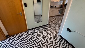 A hallway with a geometric patterned floor, a wooden door, a mirror, and a kitchen area with cabinets and appliances. - Pfullingen 1 – Accommodation for Workers, Worker House Single Rooms, Wi-Fi (Pfullingen)