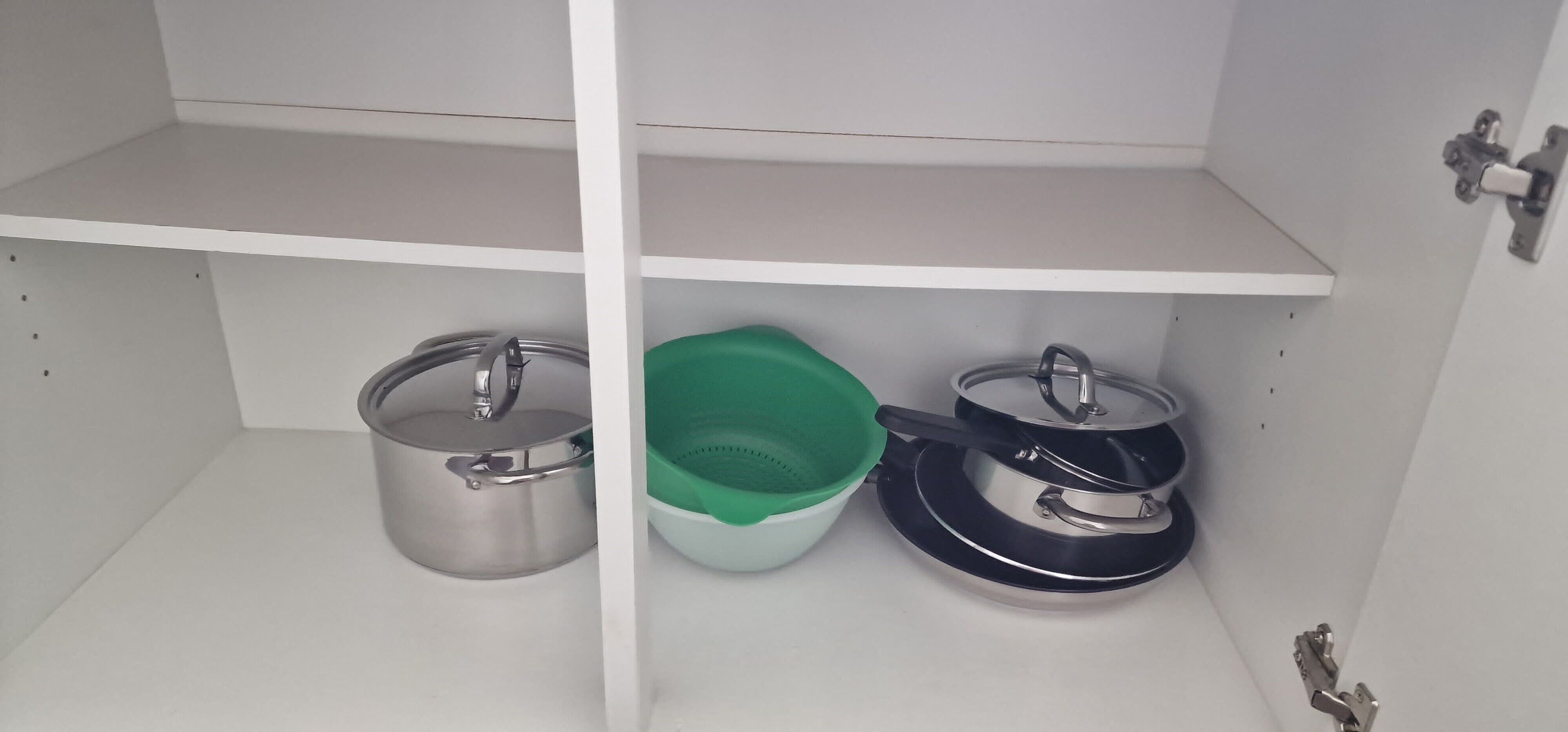 Un armario de cocina con ollas de acero inoxidable y un recipiente de plástico verde.