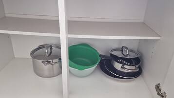 Un armario de cocina con ollas de acero inoxidable y un recipiente de plástico verde.