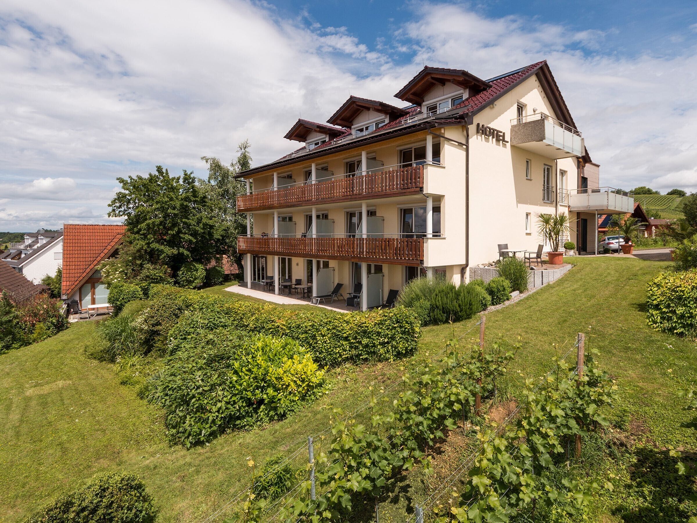 A multi-story hotel with balconies, a garden, and a hilly landscape.