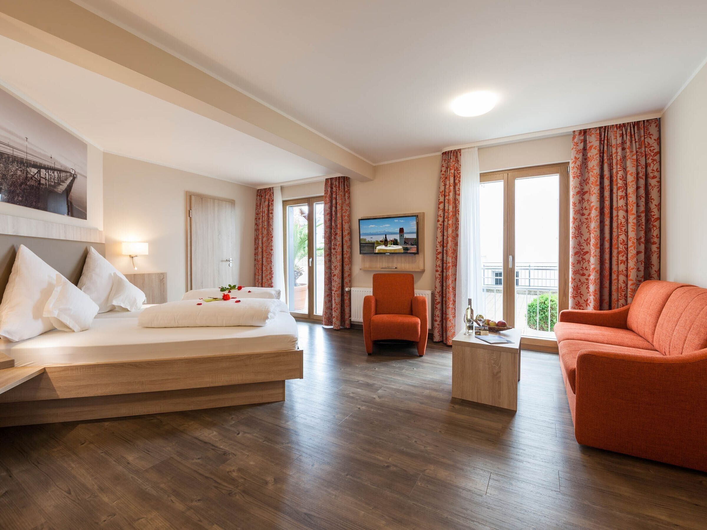 Ein Hotelzimmer mit Bett, einer Couch, einem Sessel, einem Fernseher und einem Balkon mit Vorhängen.