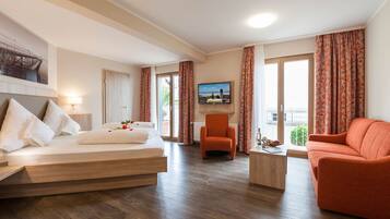 Ein Hotelzimmer mit Bett, einer Couch, einem Sessel, einem Fernseher und einem Balkon mit Vorhängen.