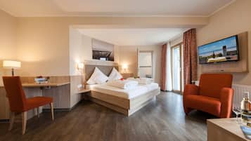 A hotel room with a bed, two armchairs, a desk, a television, and a window with curtains.
