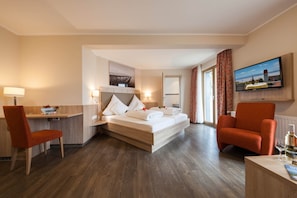 Ett hotellrum med en säng, två fåtöljer, ett skrivbord, en tv och ett fönster med gardiner.