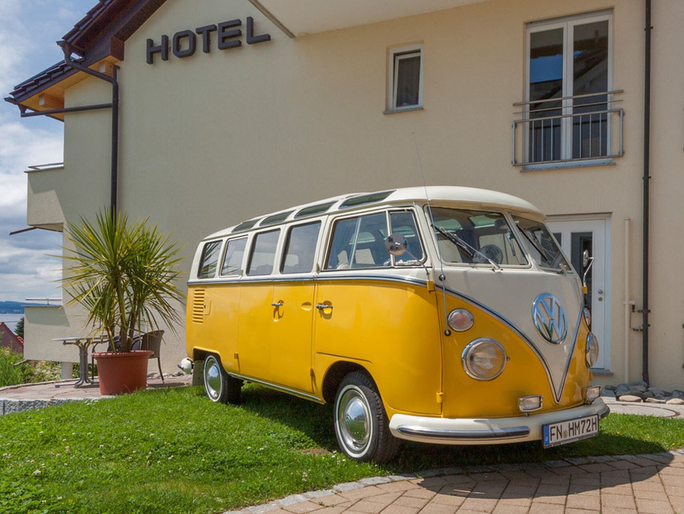 Un camper Volkswagen VW vintage giallo e bianco parcheggiato di fronte a un edificio con un cartello che recita 'HOTEL'.
