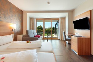 Une chambre d’hôtel comprenant un lit, un canapé, un bureau, une télévision et une porte-fenêtre coulissante donnant sur un espace extérieur.