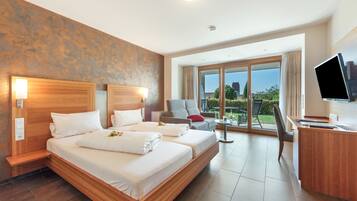 A hotel room with a large bed, a desk, a TV, and a balcony with a view.