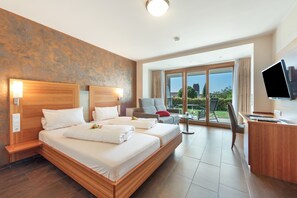 Ein Hotelzimmer mit einem großen Bett, einem Schreibtisch, einem Fernseher und einem Balkon mit Aussicht.