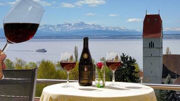Un tavolo con bicchieri da vino e una bottiglia, con vista su un lago e montagne.