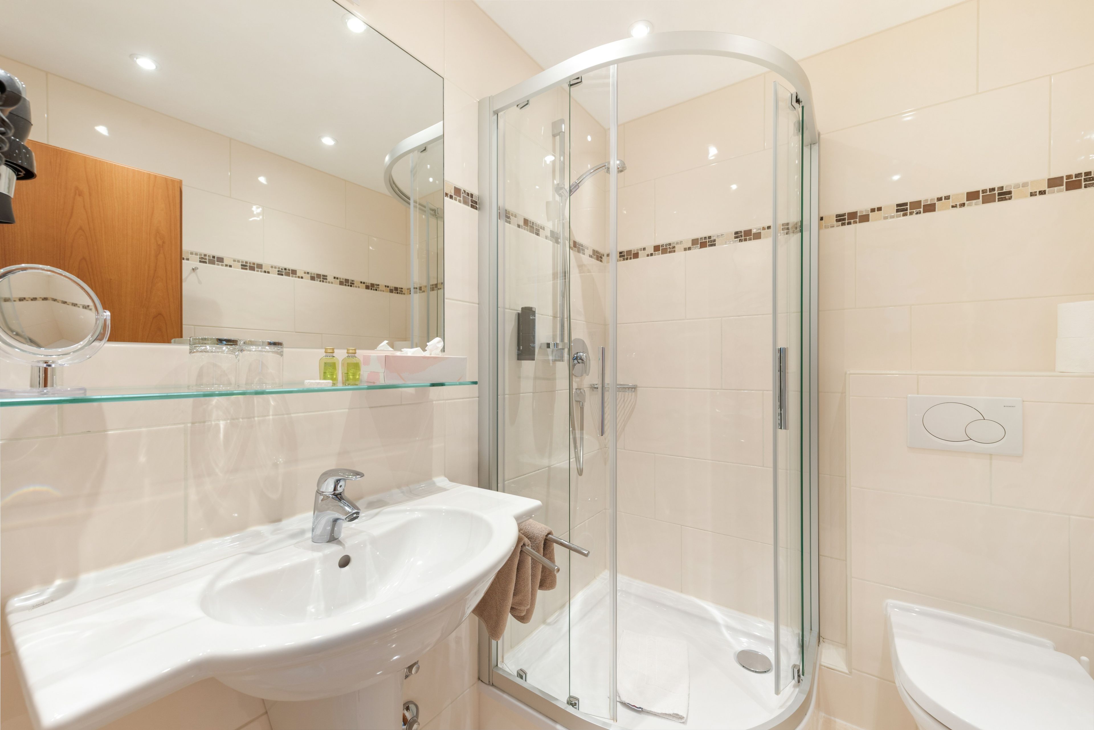 Ein modernes Badezimmer mit einer gläsernen Dusche, einem weißen Waschbecken und einem Spiegel.